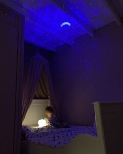 kind ligt in bed met de snoezel projector naast zich